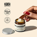 A jar of Kloris High Strength CBD Balm, with the lid off, showing the white balm inside. The label on the jar indicates it is a luxury CBD balm with 800mg CBD.