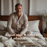 Man sitting on a bed wearing pajamas with a quote about a quiet mind and refreshed morning.